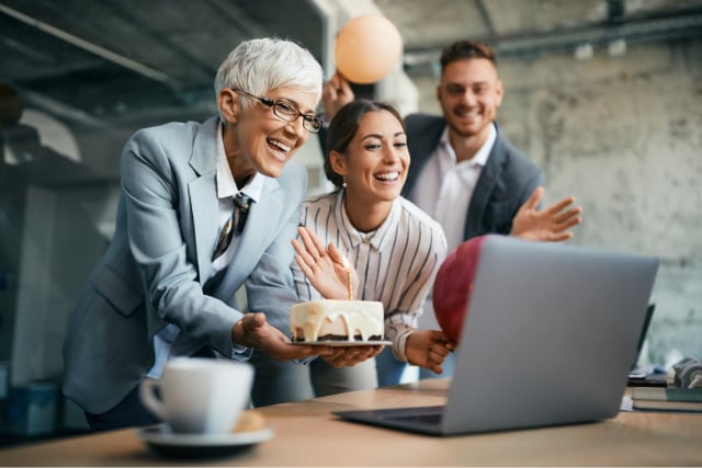 CEO with birthday cake celebrating with virtual and in-person employees