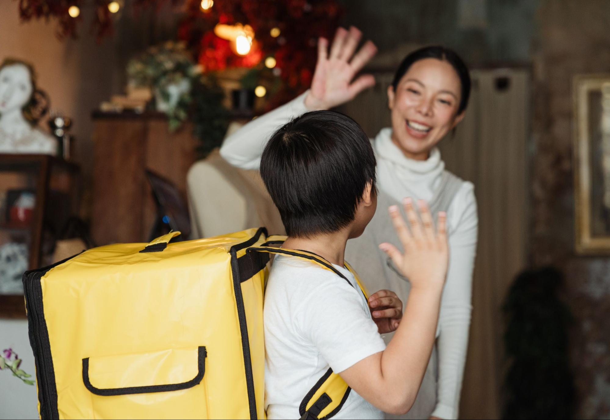 Person waving goodbye to child at door